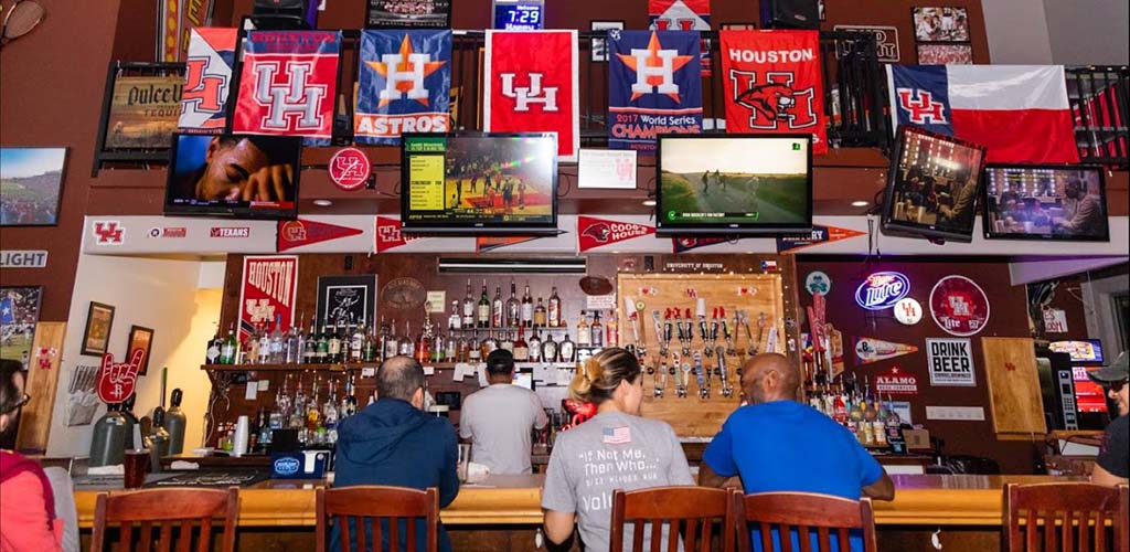 The bar of The Den Campus Pub decorated with sports flags