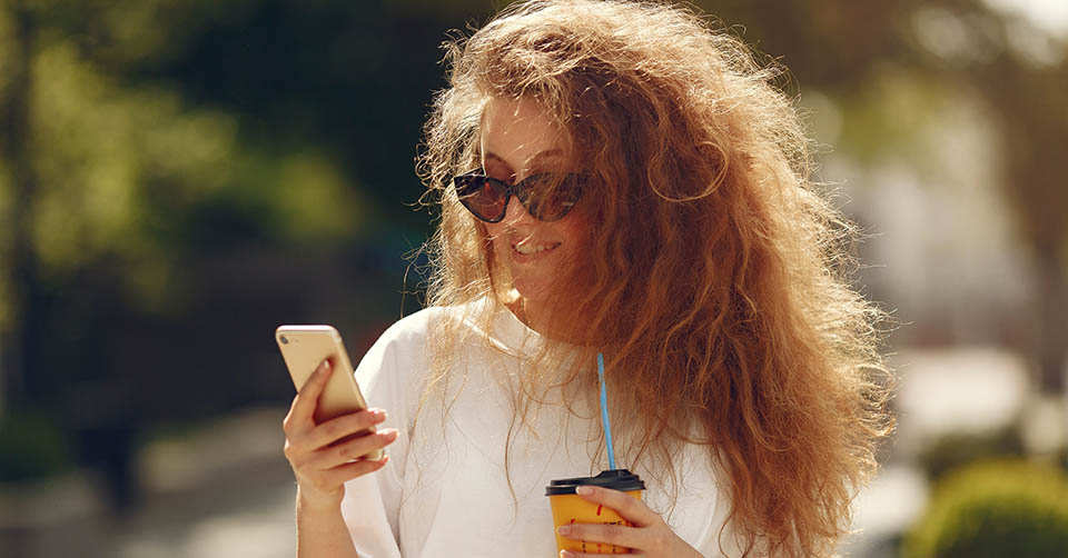 Woman in shades using a dating app while drinking coffee