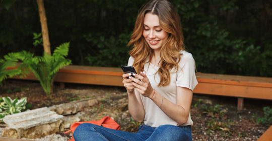 A blonde woman using the top Tulsa dating apps in a park