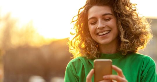 A woman with curly hair smiling while texting