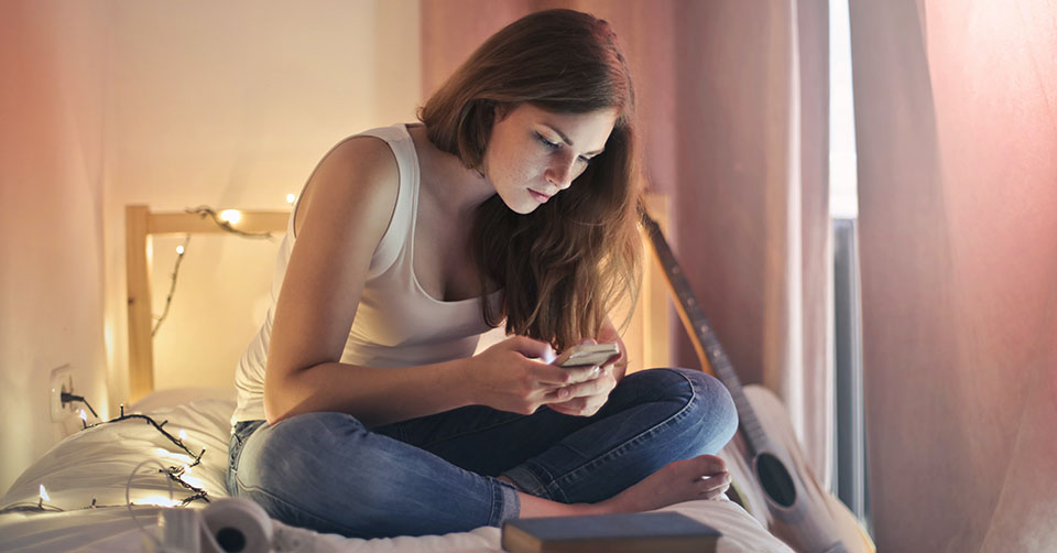 A young woman using a free dating app in bed