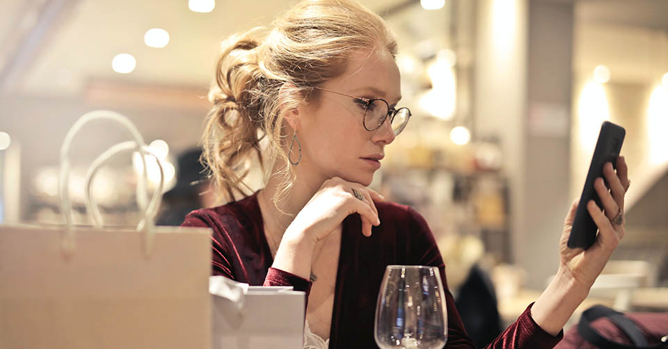 Blonde woman using a dating app while drinking wine