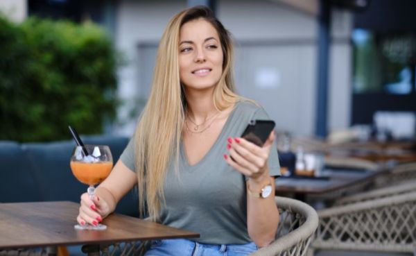 Blonde woman checking out Wollongong dating apps while drinking a cocktail