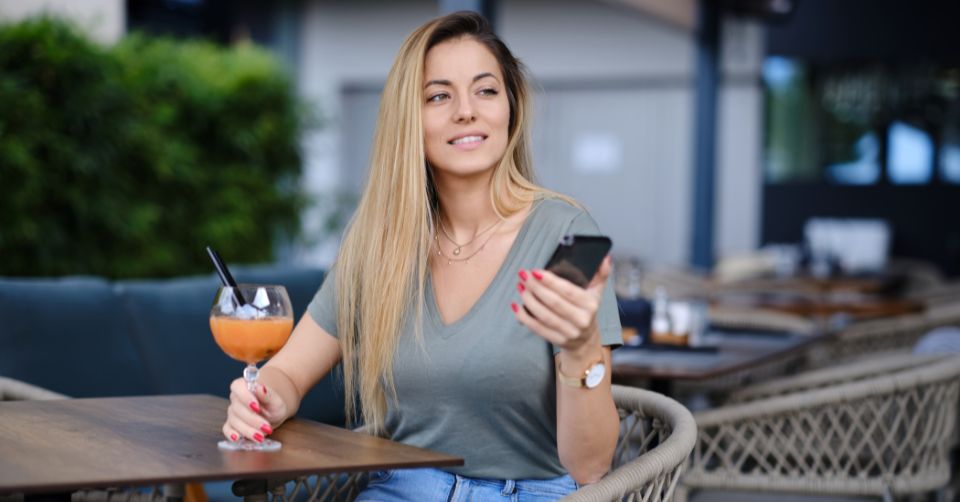 Blonde woman checking out Wollongong dating apps while drinking a cocktail