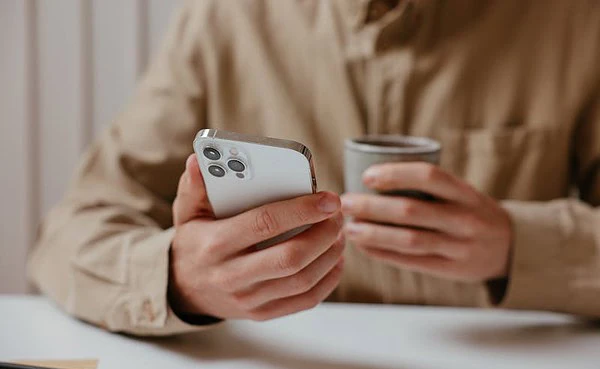 Man checking a dating app on his phone while holding a coffee cup