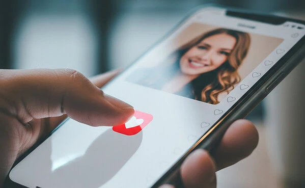 Young man taping a heart symbol on smartphone, representing modern online dating.