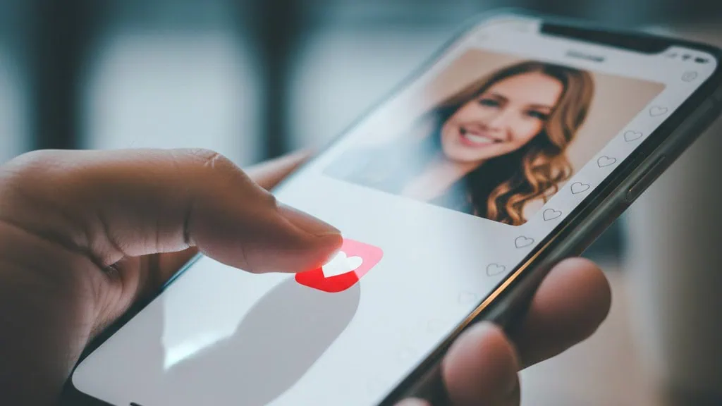 Young man taping a heart symbol on smartphone, representing modern online dating.