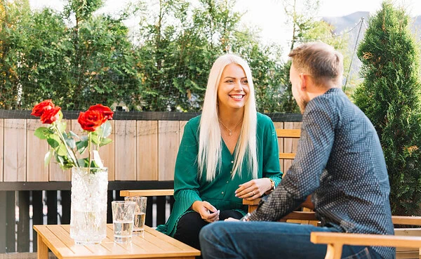 A mature woman and younger man laugh together over coffee at an outdoor café, showcasing a joyful connection on a milf dating app.