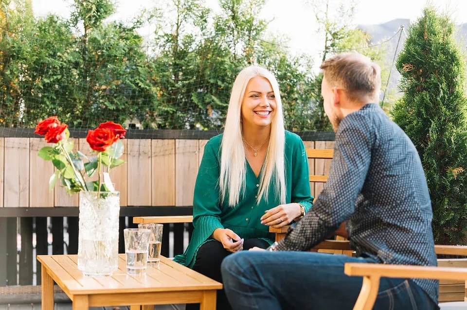 A mature woman and younger man laugh together over coffee at an outdoor café, showcasing a joyful connection on a milf dating app.