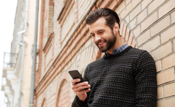 Young man smiling at phone screen with attractive mature woman's profile on a MILF dating app, evoking easy online connections for beginners.