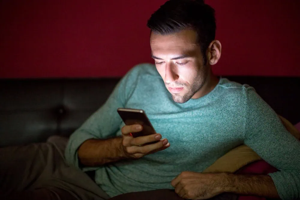 Young man scrolling through dating apps on his phone at midnight, wondering if the next match will deliver real connections.